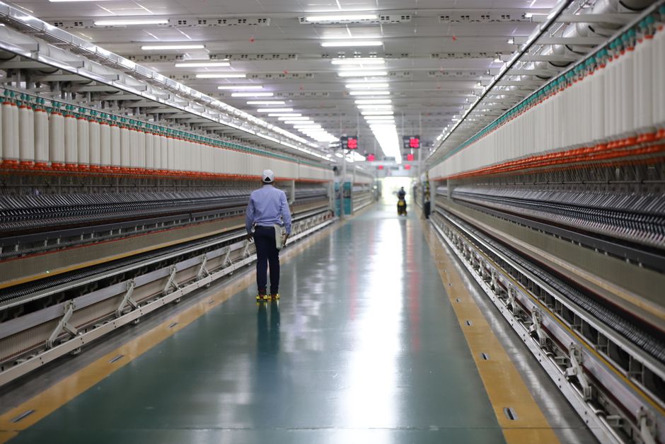 A worker walks through a wide hallway in an industrial textile plant, India, Huizhou, Guangdong