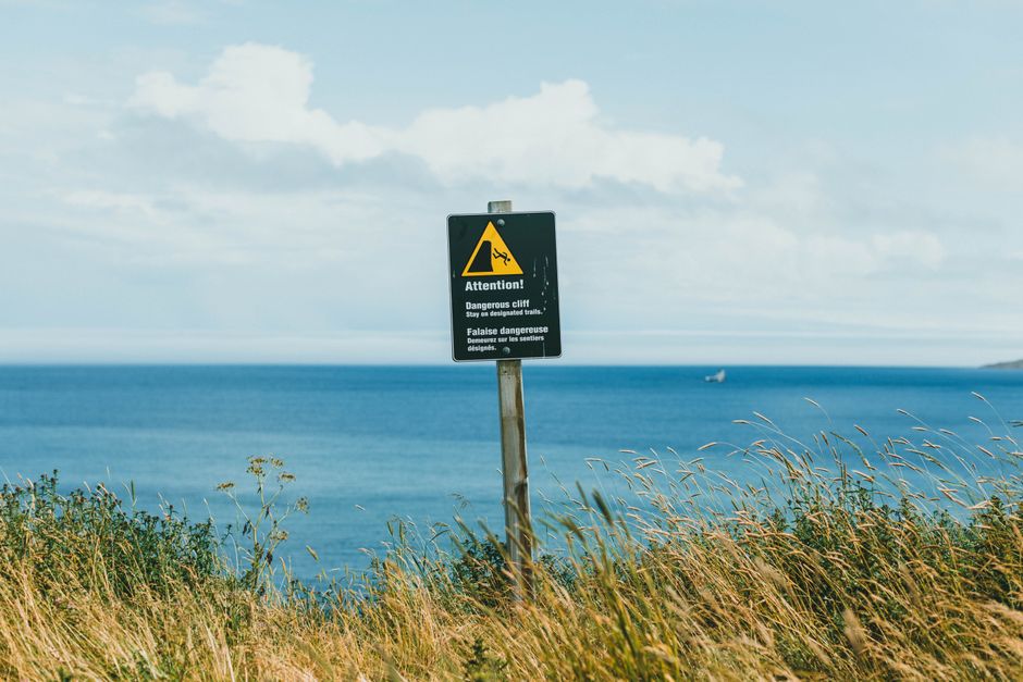 A warning sign on a coastal cliff, with a view of the ocean on a clear day, Huizhou, Guangdong
