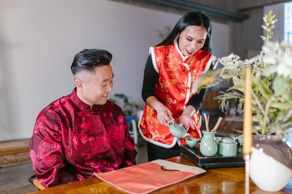 An Asian couple enjoys a traditional tea ceremony indoors, showcasing vibrant traditional attire.