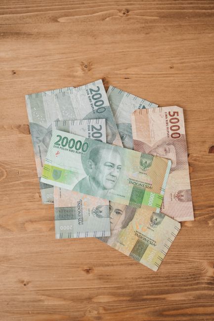 Close-up of Indonesian Rupiah banknotes scattered on a wooden table, showcasing various denominations.