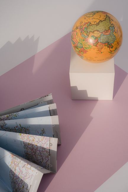 A globe and a folded paper map on a pink surface with shadows creating a conceptual travel theme.