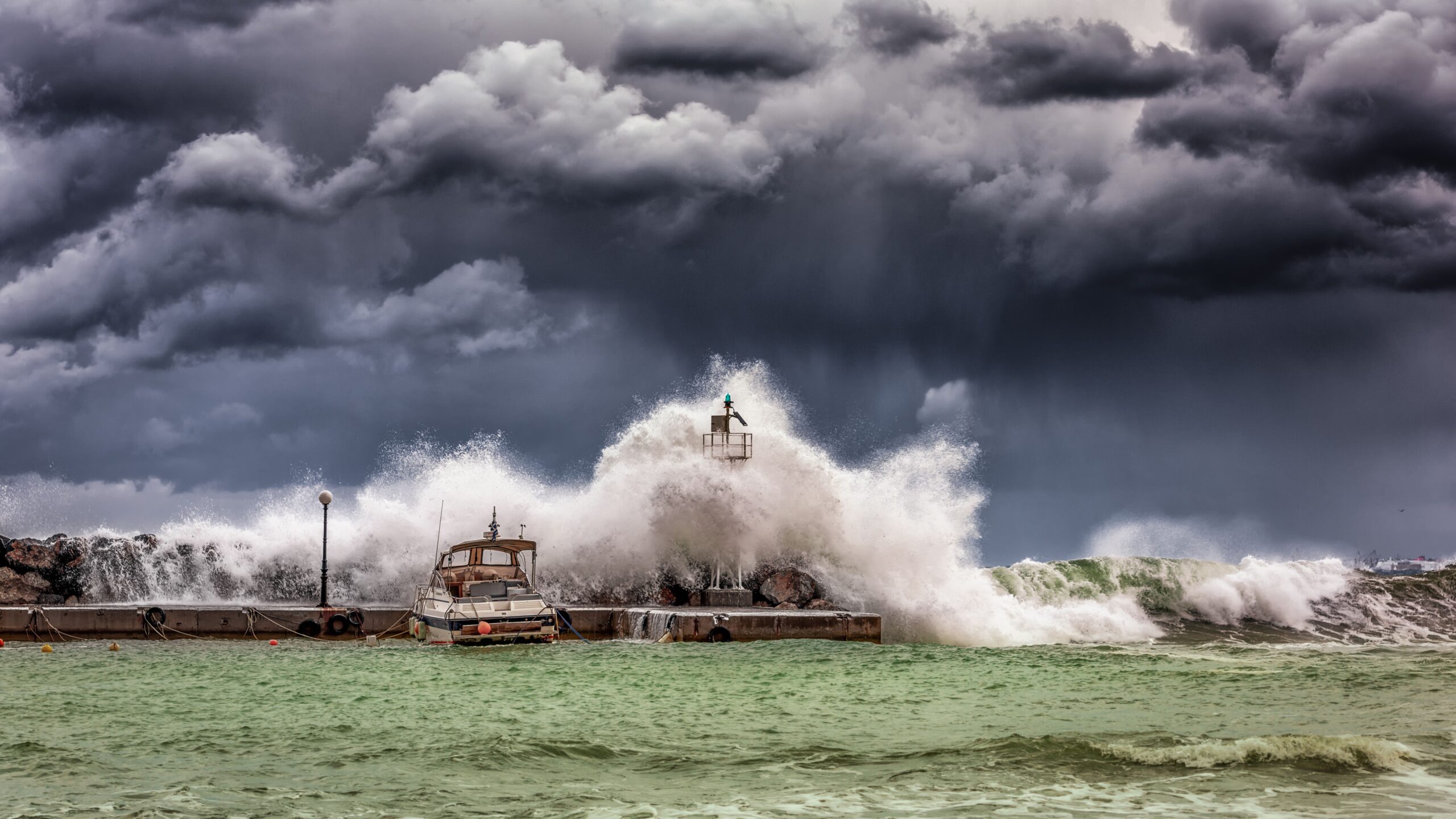 Powerful waves crash against a pier and lighthouse under dark stormy skies. — Huizhou, Guangdong, China