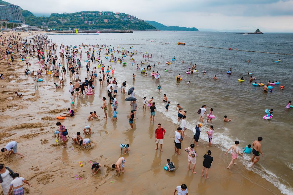 A lively scene at Dameisha Beach, Shenzhen, with people enjoying summer leisure activities by the sea. — Huizhou,