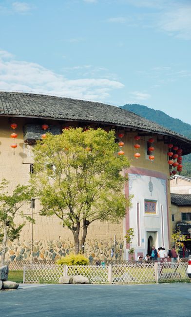 Scenic view of a traditional Huizhou Tulou with red lanterns surrounded by nature.