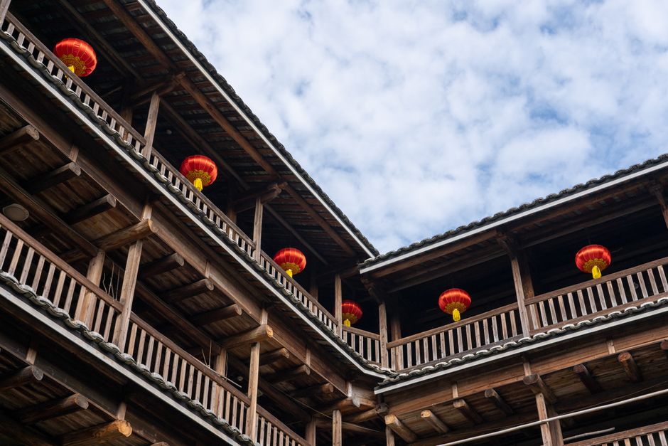 Wooden Tulou building with vibrant red lanterns under a blue sky, showcasing traditional Chinese architecture. —