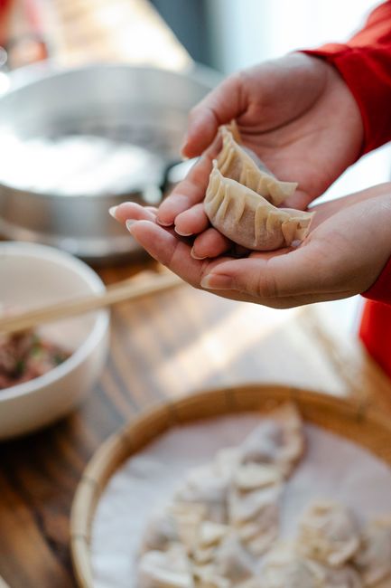 From above of crop faceless woman showing folded raw homemade jiaozi dumplings while standing in kitchen in daylight —