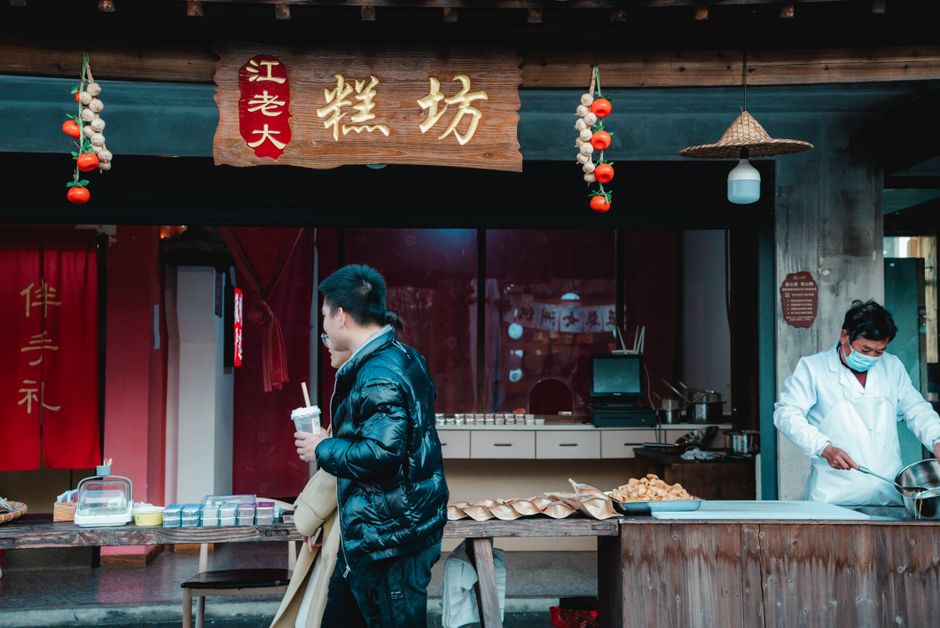 A bustling street food stall offering traditional dishes to a customer in stylish winter attire. — Huizhou, Guangdong,